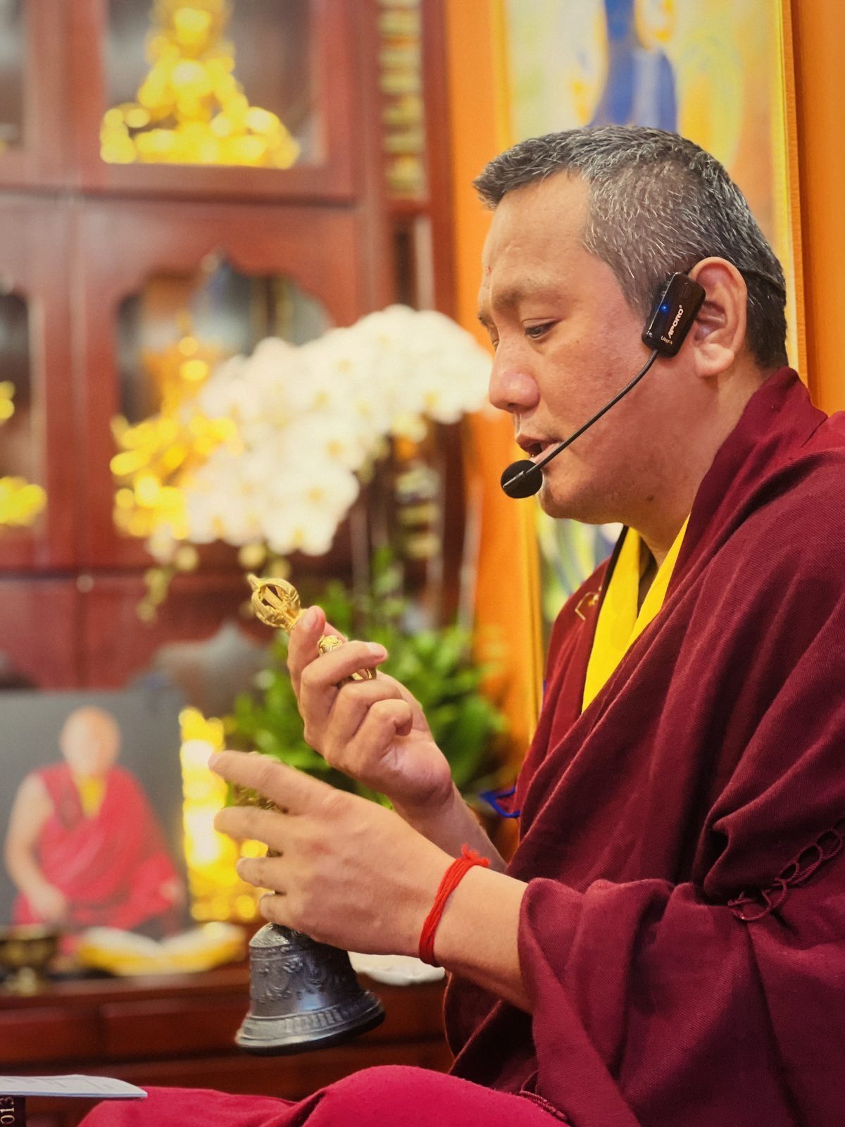 Rinpoche cầm chày và chuông kim cương, giảng pháp tại trung tâm; phía sau là ảnh Đức Pháp Vương Chetsang